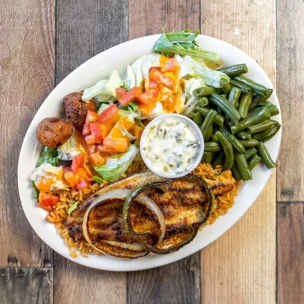 Grilled fish with rice, green beans, salad, hushpuppies, and tartar sauce on a white plate.