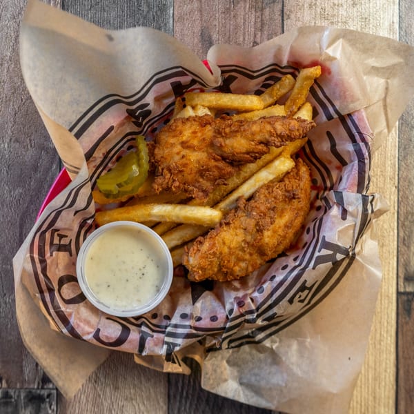 River Smith's fried catfish and fries in a basket with a side of tartar sauce and pickles.