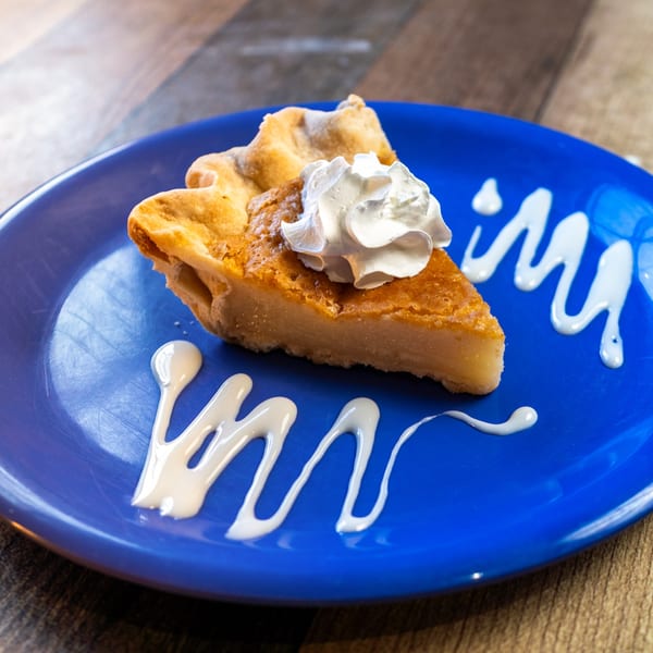A slice of River Smith's sweet potato pie with whipped cream on a blue plate.