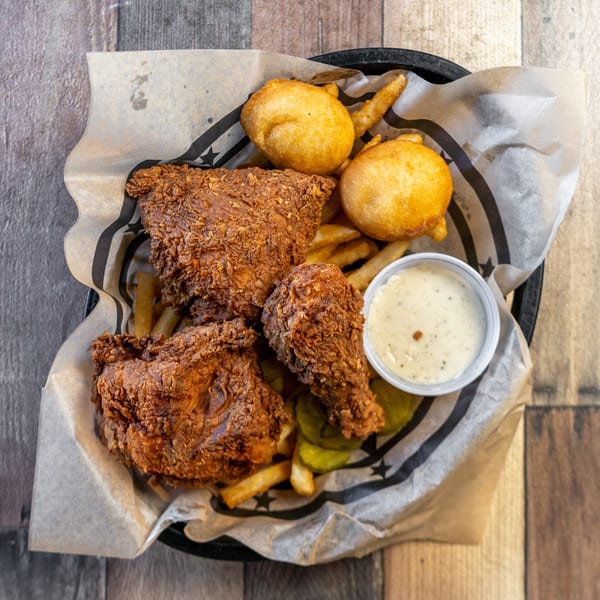 River Smith's fried chicken, hushpuppies, fries, pickles, and dipping sauce in a basket.