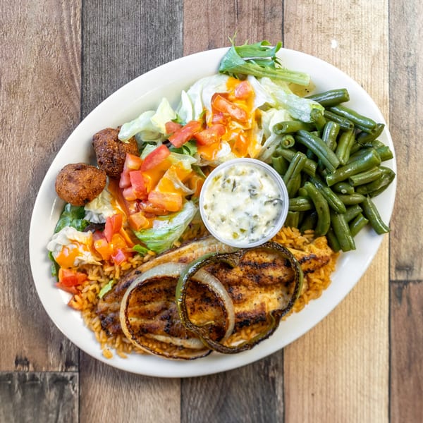 Grilled catfish with rice, green beans, salad, hushpuppies, and tartar sauce on a white plate.