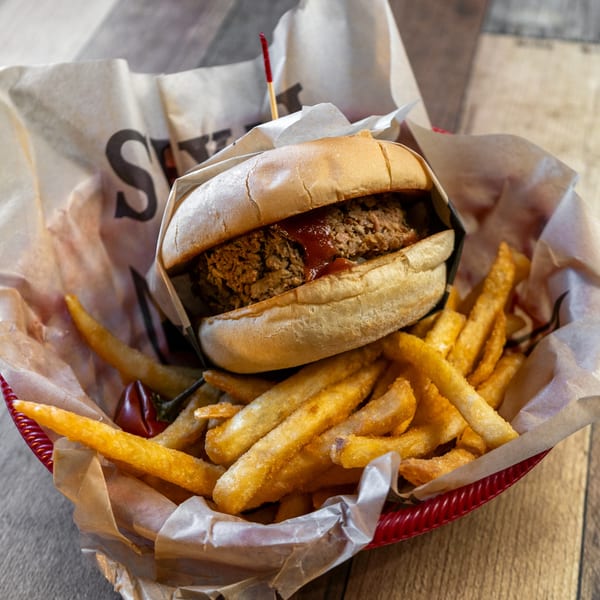 River Smith's pulled pork sandwich with barbecue sauce and a side of french fries in a red basket.